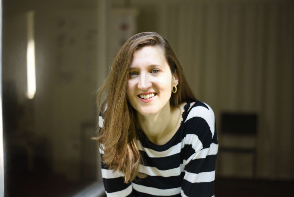 Martina Rick, Vocal und Performance Coach, schaut im schwarz-weiss-gestreiften Shirt lächelnd aus dem offenen Fenster ihres Studios in Basel