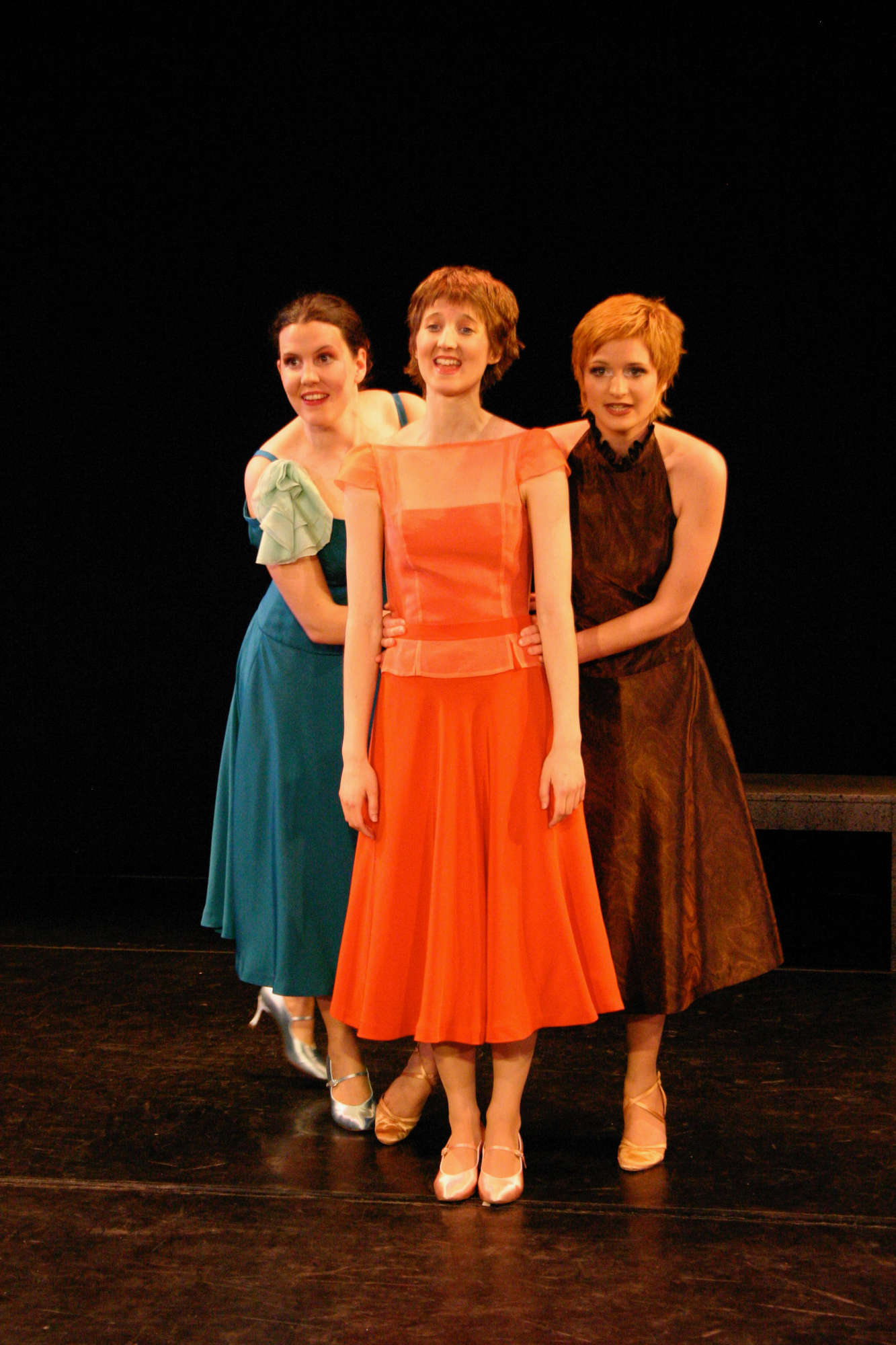 Martina Rick in orangenem Kleid auf der Bühne mit zwei weiteren Darstellerinnen in einer Aufführung des Stücks "Pretty Women" 2004