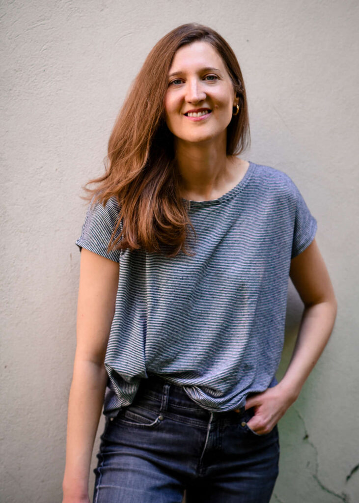 Martina Rick in gestreiftem T-Shirt vor der weissen Aussenwand ihres Studios für Gesangsunterricht in Basel